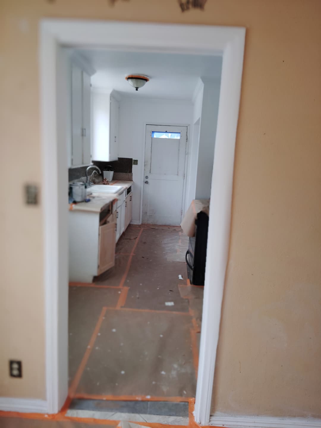 Kitchen prepped for painting with floors covered and cabinets masked off