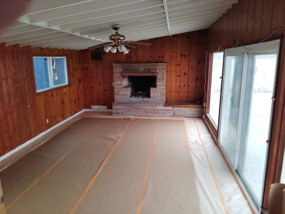 Wood paneled living room with fireplace fully covered and ready for painting