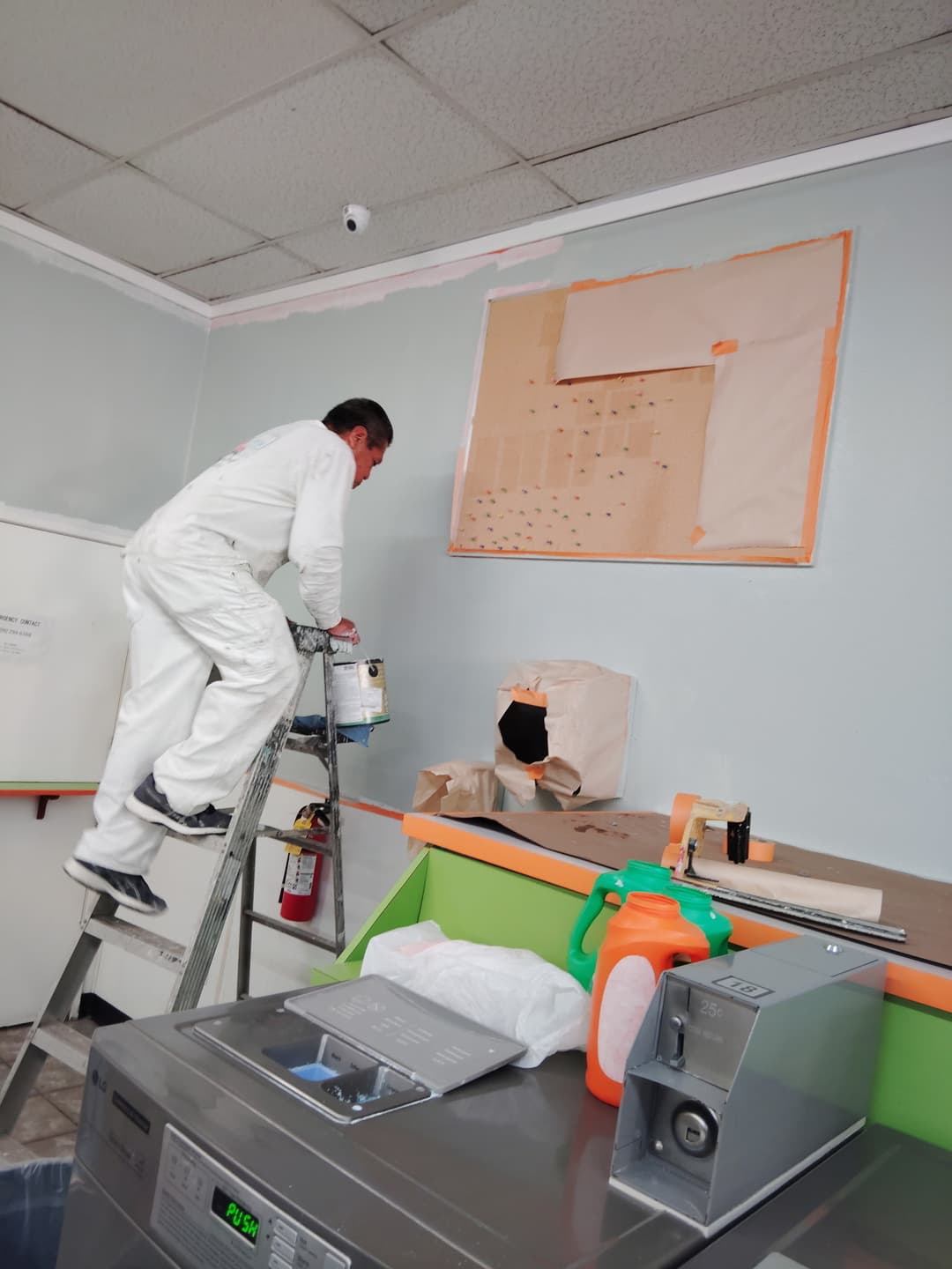 Professional painter on a ladder cutting in wall paint in a commercial interior